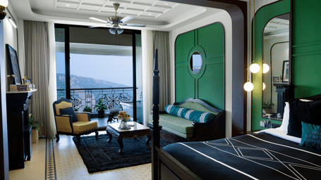 Waterfall Deck Suite at Polo Resort Cherrapunji with four-poster bed, green-panelled wall, balcony seating area and valley view through doors.