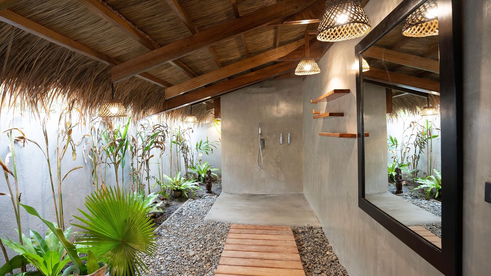 Outdoor shower area at Flower Island Resort with concrete walls, a shower head, and surrounding greenery.