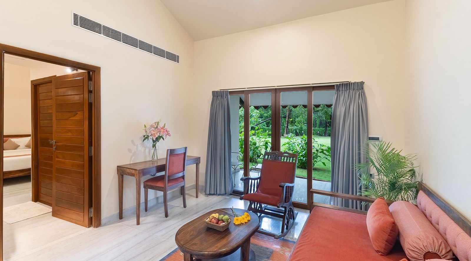 image of the separate living area featuring an orange couch with beautiful green view of the lawn from the windows at the luxury suite villa at aranya vilas