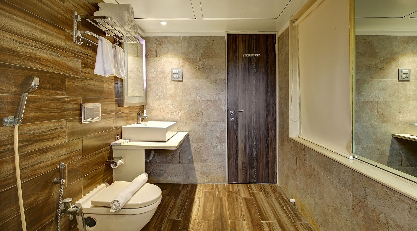 Bathroom with toilet, square basin, mirror, wooden and beige tiles, and a door.