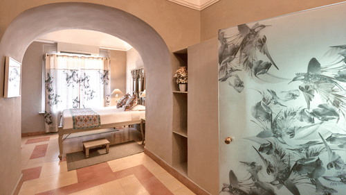 A hallway with an arched doorway leading to another room, featuring a decorative glass door and a built-in shelf in Tijara Fort-Palace - 19th Century, Alwar.