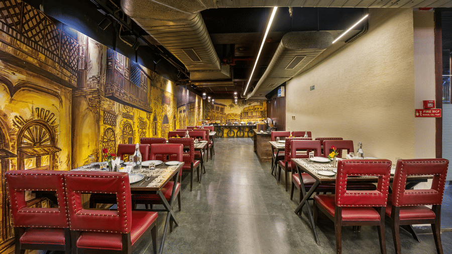 Wide view of the restaurant dining hall at Lords Inn Amritsar with red and green chairs, ornate wall murals, and warm overhead lighting.