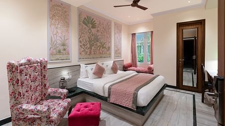 A spacious bedroom at Panna Vilas Palace, complete with a wooden table, cushioned furniture, warm lighting, and a large window