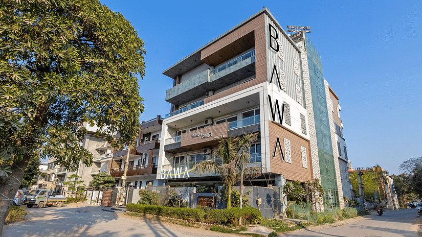 Exterior view of  the facade of Hotel Bawa, Gurgaon, a multi-storeyed building with a tree in the foreground and a clear blue sky in the background.