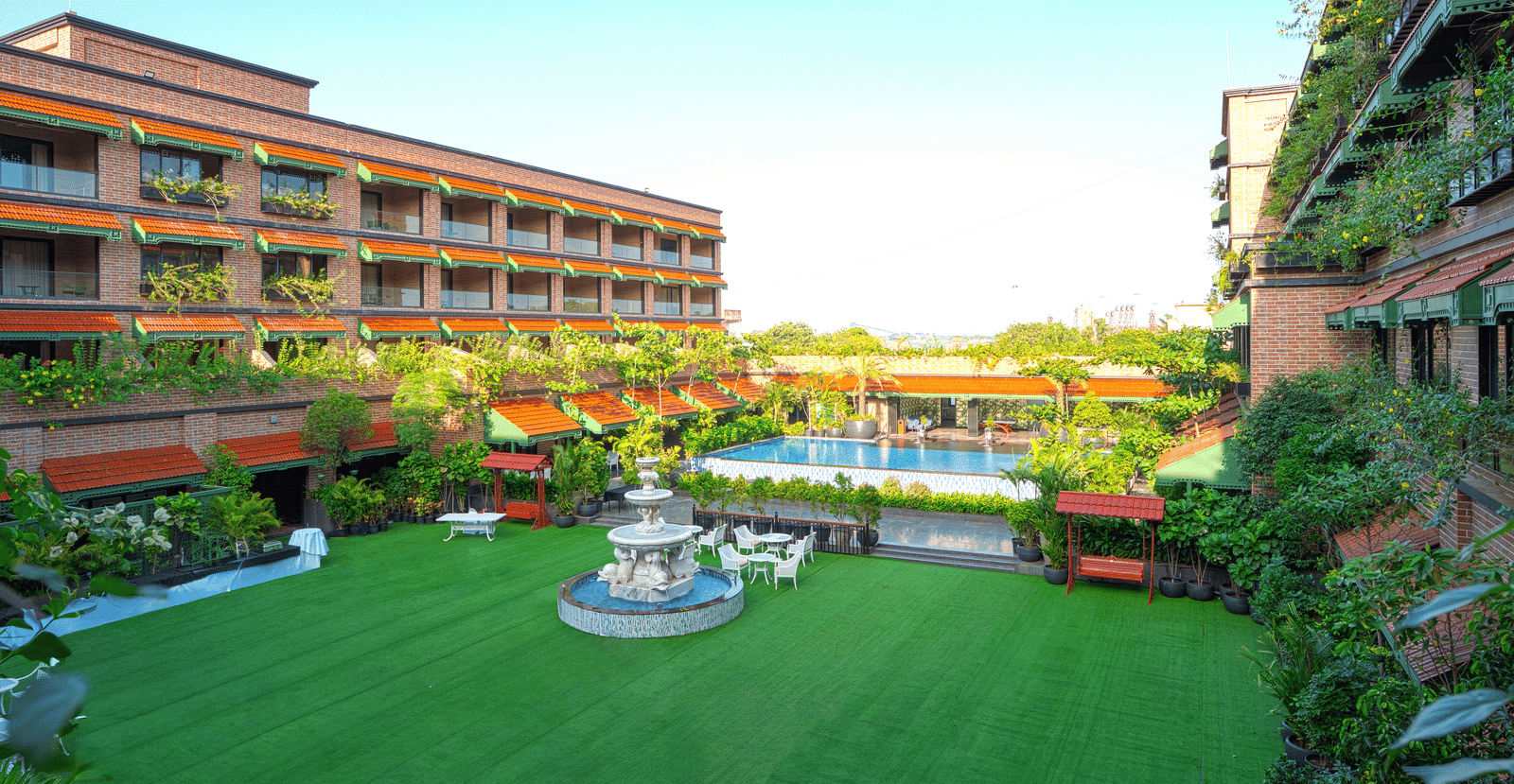 Outdoor lawn with pathways, seating areas, fountain, greenery, and multi-storey building of MAYFAIR Bay Resort, Paradeep.