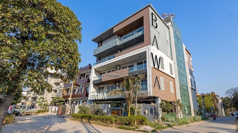 Exterior view of  the facade of Hotel Bawa, Gurgaon, a multi-storeyed building with a tree in the foreground and a clear blue sky in the background.