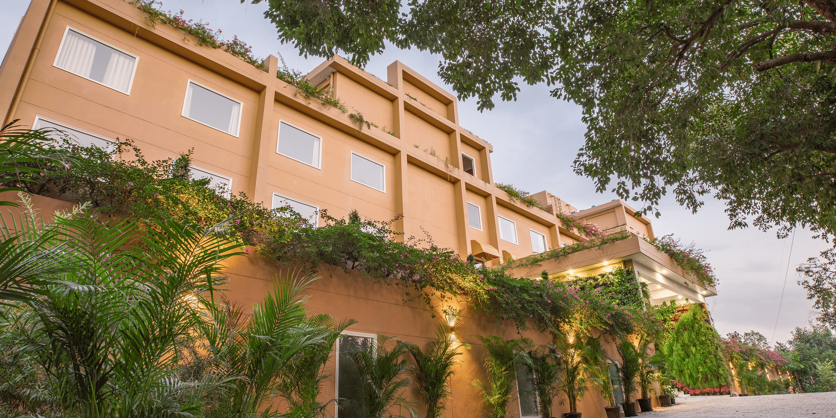 The facade of Lalitha Grand, featuring plants infront of the building.