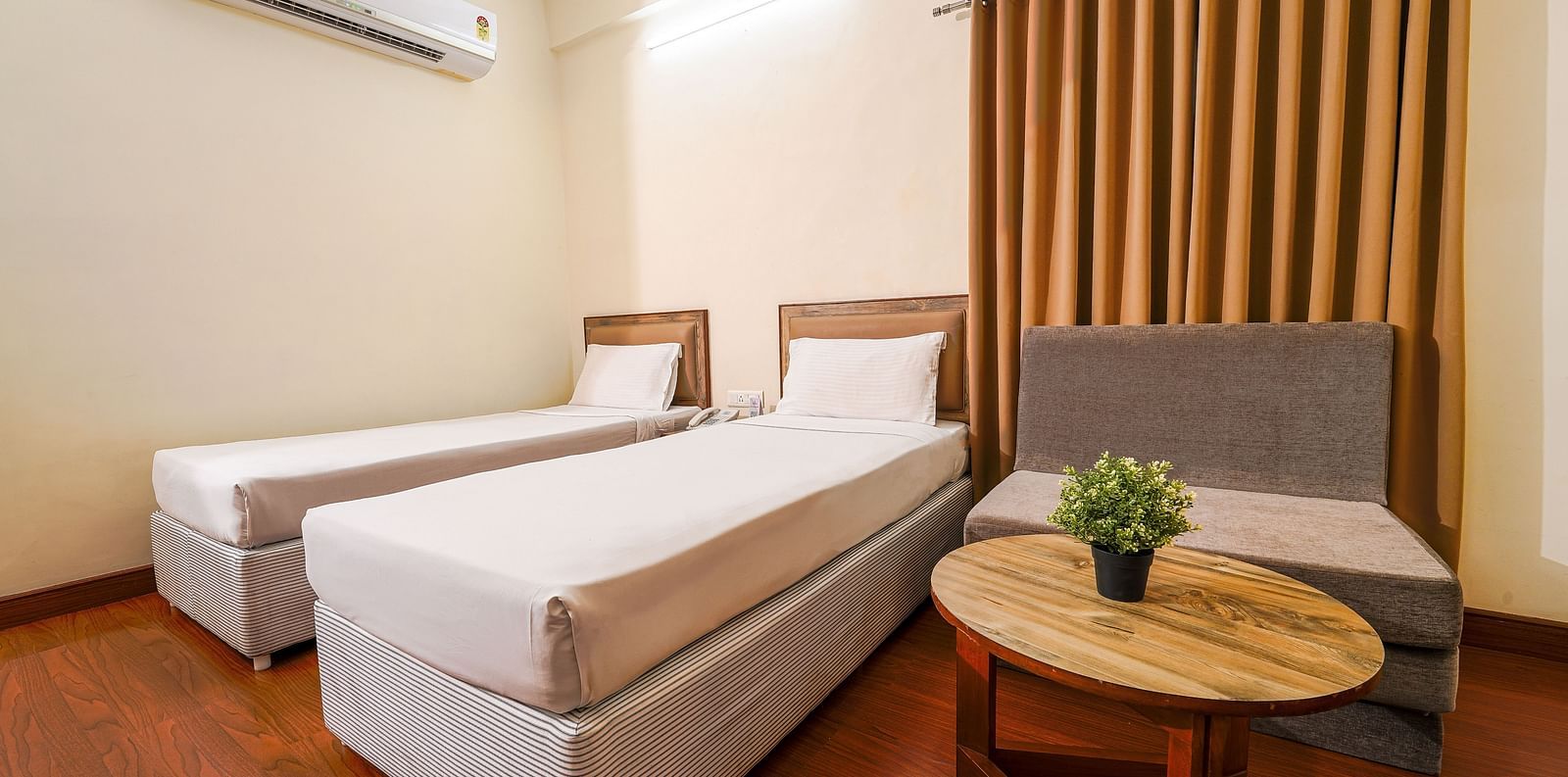 Hotel room with two single beds, wooden flooring, and a comfortable seating area in Hyderabad near Ramoji Film City.