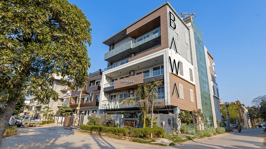 Exterior view of  the facade of Hotel Bawa, Gurgaon, a multi-storeyed building with a tree in the foreground and a clear blue sky in the background.