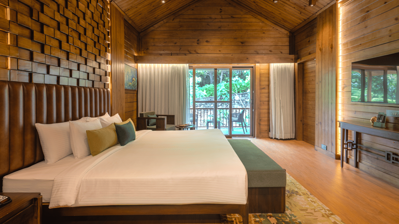 Premium Wooden Cottage with Bathtub bedroom featuring a wooden accent wall and garden view at The Ananta Udaipur.