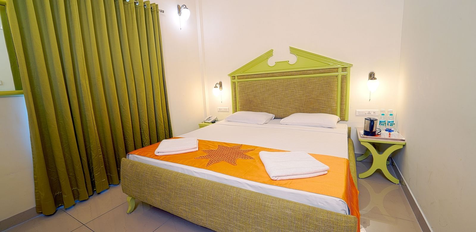A hotel bedroom with a large double bed, green headboard, and green curtains, giving a cozy ambience at Greens Inn - Best Accommodation in Ramoji Film City.
