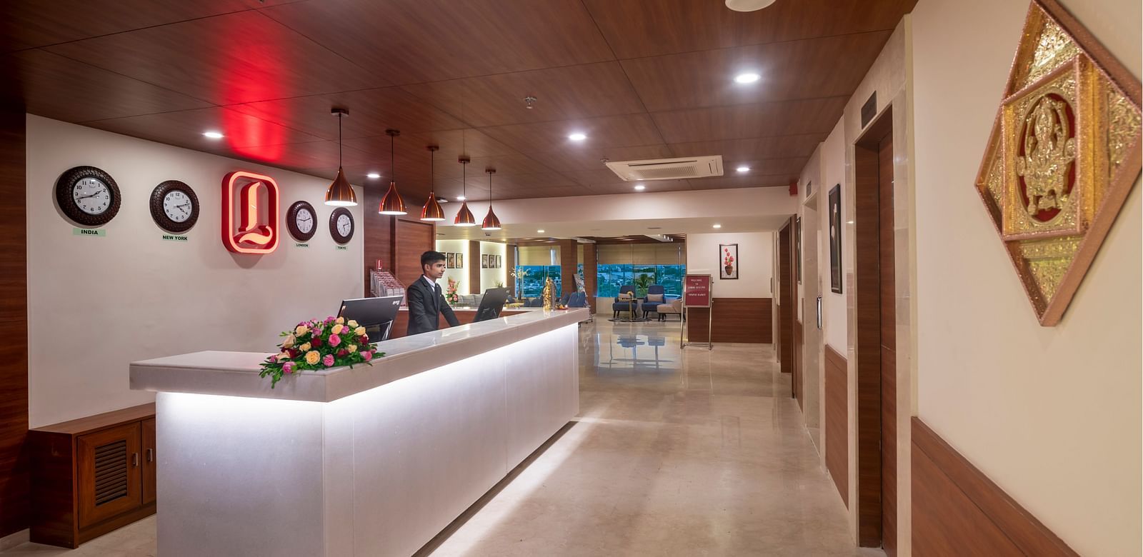 A hotel lobby with a reception desk, decorative clocks on the wall, and a hallway leading to guest rooms.