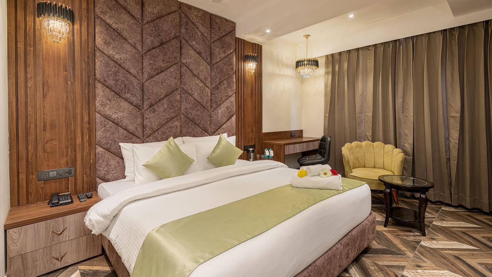 Deluxe Room at DLS Grand Luxotica, Dehradun showcasing a plush bed with a nightstand next to it and a sitting space on the other side next to the window with a couch and coffee table