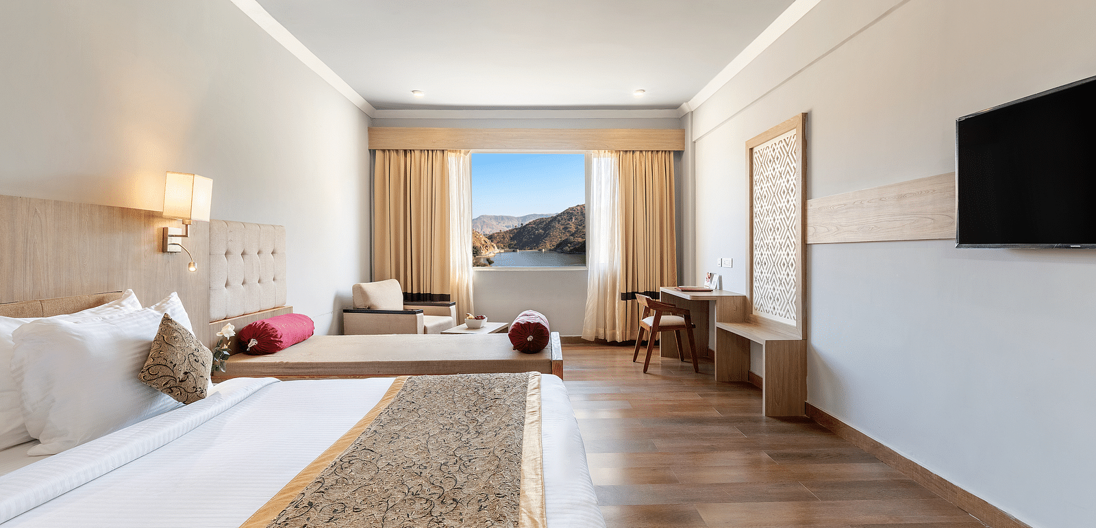 A close-up shot of a bed with a patterned runner on it, opposote to it is a tv mounted on the wall -  Via Lakhela Resort & Spa 