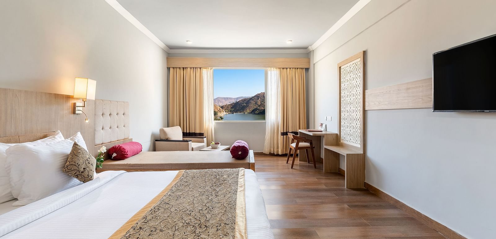 A close-up shot of a bed with a patterned runner on it, opposote to it is a tv mounted on the wall -  Via Lakhela Resort & Spa 