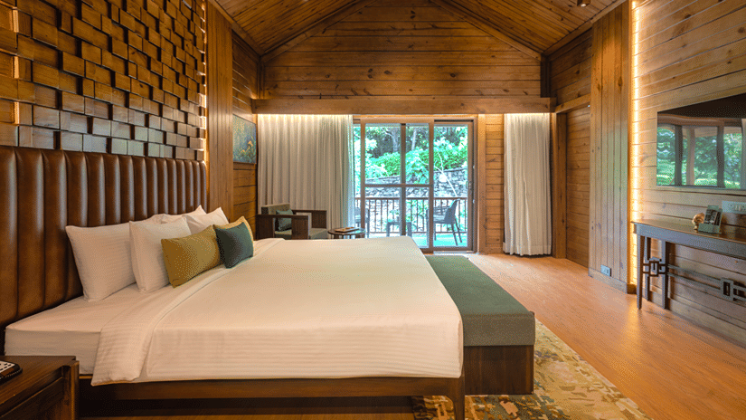 Premium Wooden Cottage with Bathtub bedroom featuring a wooden accent wall and garden view at The Ananta Udaipur.