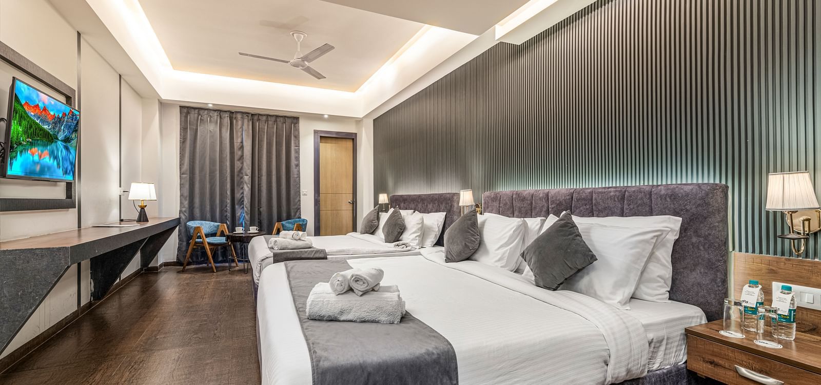 A mirror shot of a room at DLS Ganga Bliss, Haridwar with two king size beds facing a flat screen TV mounted on a wall
