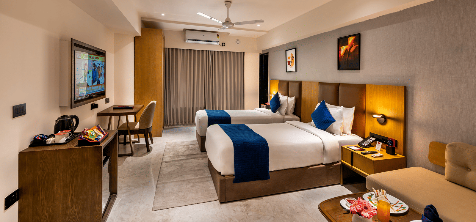 Elegantly furnished deluxe room with a king-sized bed, blue accent pillows, and warm lighting at Lords Studio Inn, Jamnagar.