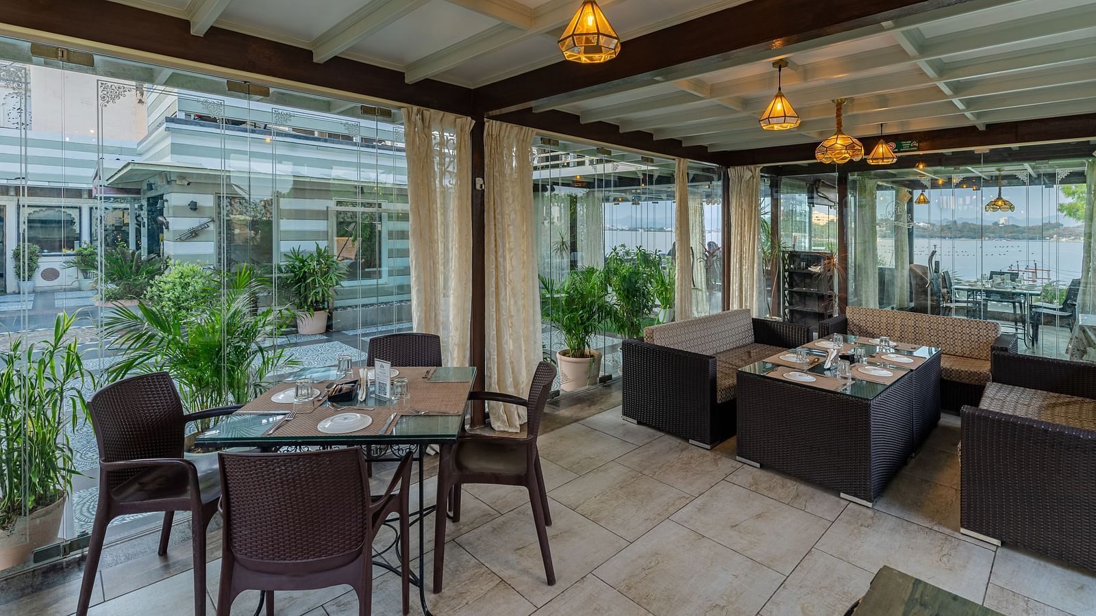 At Panna Vilas Palace, the restaurant area features a four-seater table with wooden chairs arranged around it, accented by warm lighting and potted plants | Panna Vilas Udaipur