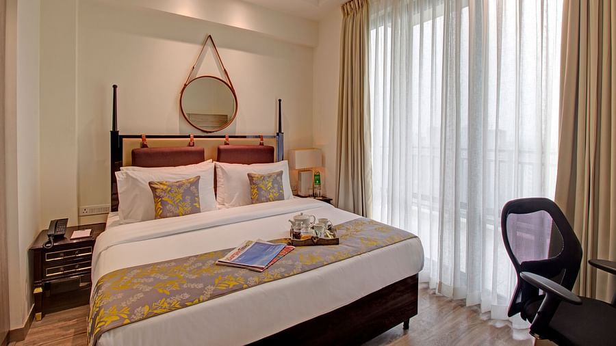 a king bed with side tables and a study table opposite it inside Deluxe Room - Rhythm Gurugram