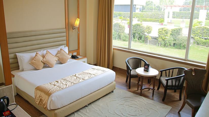 A room featuring a king-size bed next to which a set of chairs and coffee table is placed right beside the huge window
