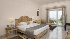 Superior Room with Balcony at Fateh Safari Resort, Kumbhalgarh featuring a double size bed, a bedside table with water bottles, a sofa with centre table, and a balcony with plunge pool with a view of the hill.
