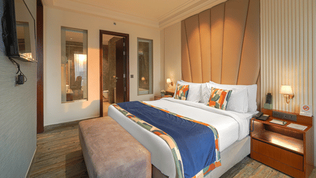 A suite at BluSalzz Residence, Amritsar, with a double bed, a cushion, tables, lamps, and a television