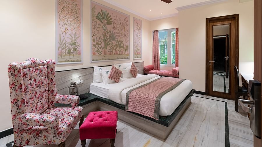 A spacious bedroom at Panna Vilas Palace, complete with a wooden table, cushioned furniture, warm lighting, and a large window