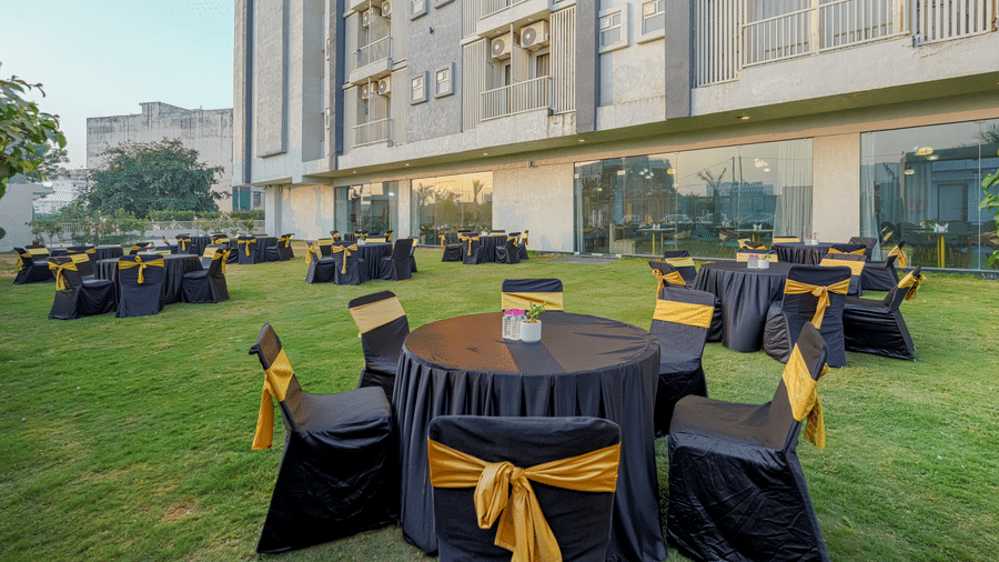 The outdoor venue at Urban Suites by BluSalzz, Jaipur, showing several set tables and chairs on the lawn adjacent to the lower level of a building with many windows.
