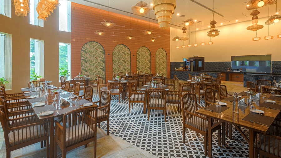 Restaurant dining area with wooden tables, upholstered chairs, pendant lighting, decorative wall panels and large windows.