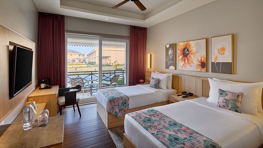 A hotel room featuring two twin beds with floral runners, a desk, a TV, and a view of a body of water through a sliding glass door -  Voyage The Solitaire Bliss.