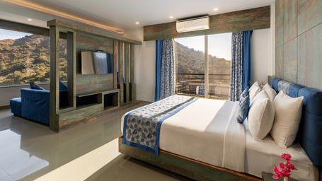 A bedroom with a made bed, patterned runner and a mountain view through the window -  Via Lakhela Lakeview Resort