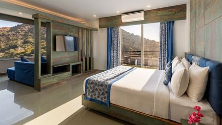 A bedroom with a made bed, patterned runner and a mountain view through the window - Via Lakhela Resort & Spa 