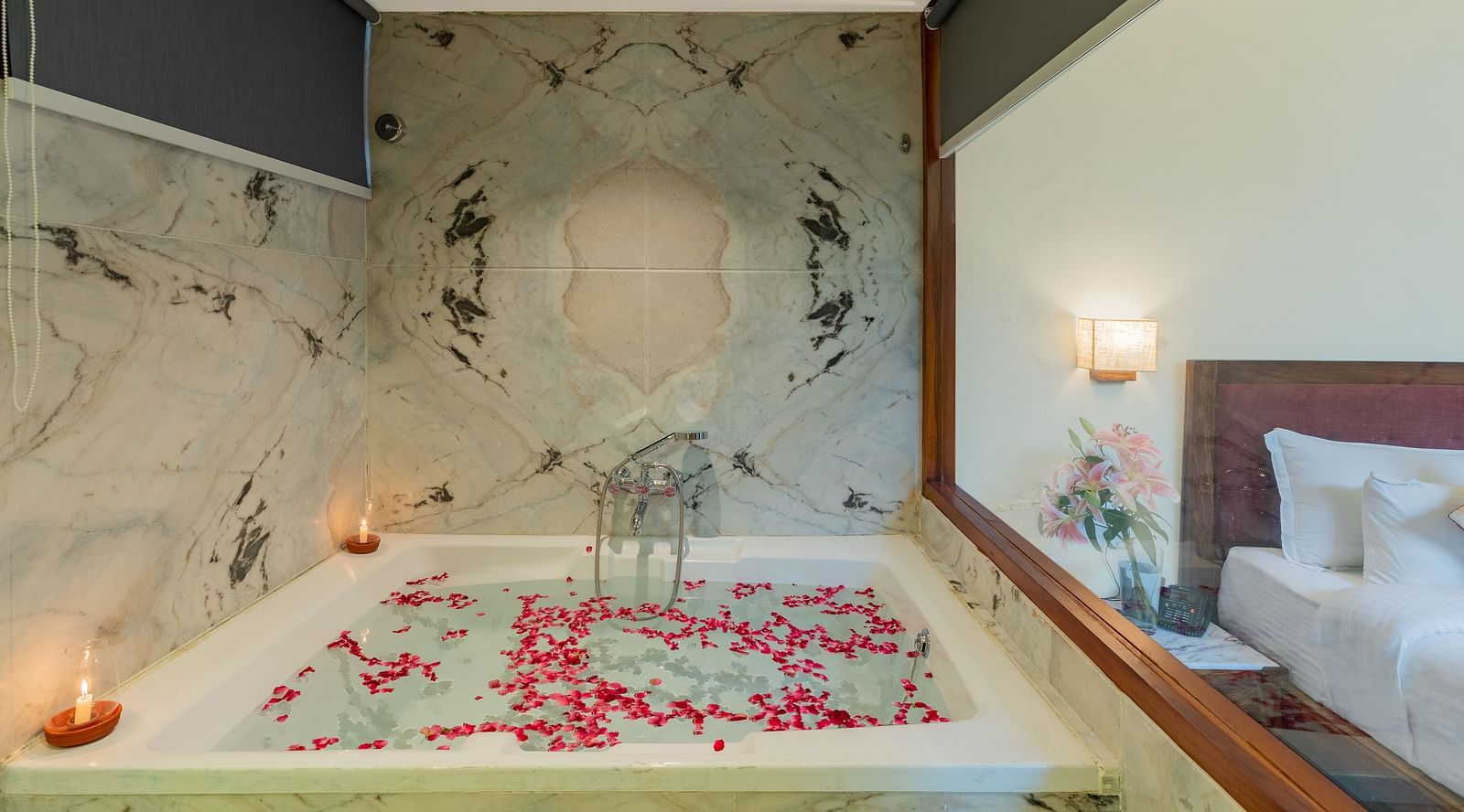 close up image of the bathtub with candles in the corner and a glass partition between the room and the bathroom in the luxury bathtub villa in aranya vilas