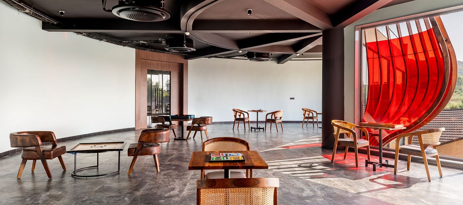 An indoor games area at The Qualia Resort Club & Brewery, Udaipur featuring unique seating arrangements, a dark ceiling with track lighting, and a partial view of a red curtain.