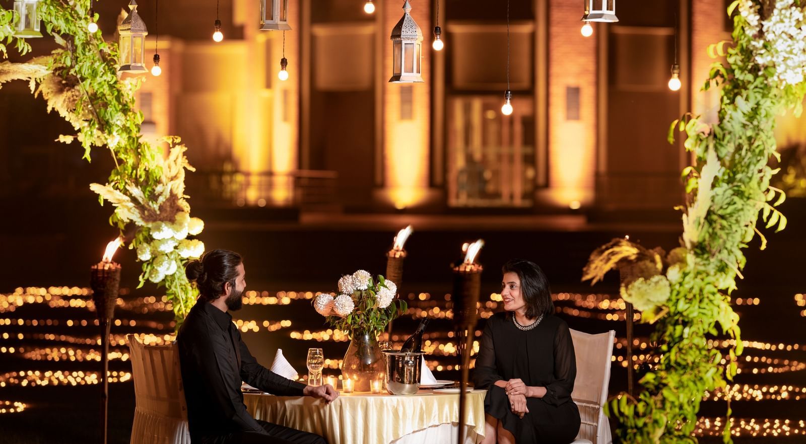A couple enjoying dinner in an open-air setting surrounded by lavish decoration at Nirvana Luxury Hotel, Ludhiana.