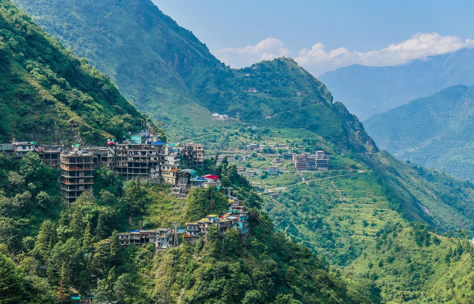 Aerial view of mountains under daylight, featuring a few buildings in the stunning natural landscape.