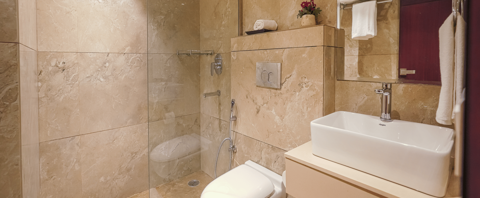 A hotel bathroom featuring marble-effect tiling, a toilet, a square basin, and a glass partition for the shower area at BluSalzz Select City Centre, Amritsar.