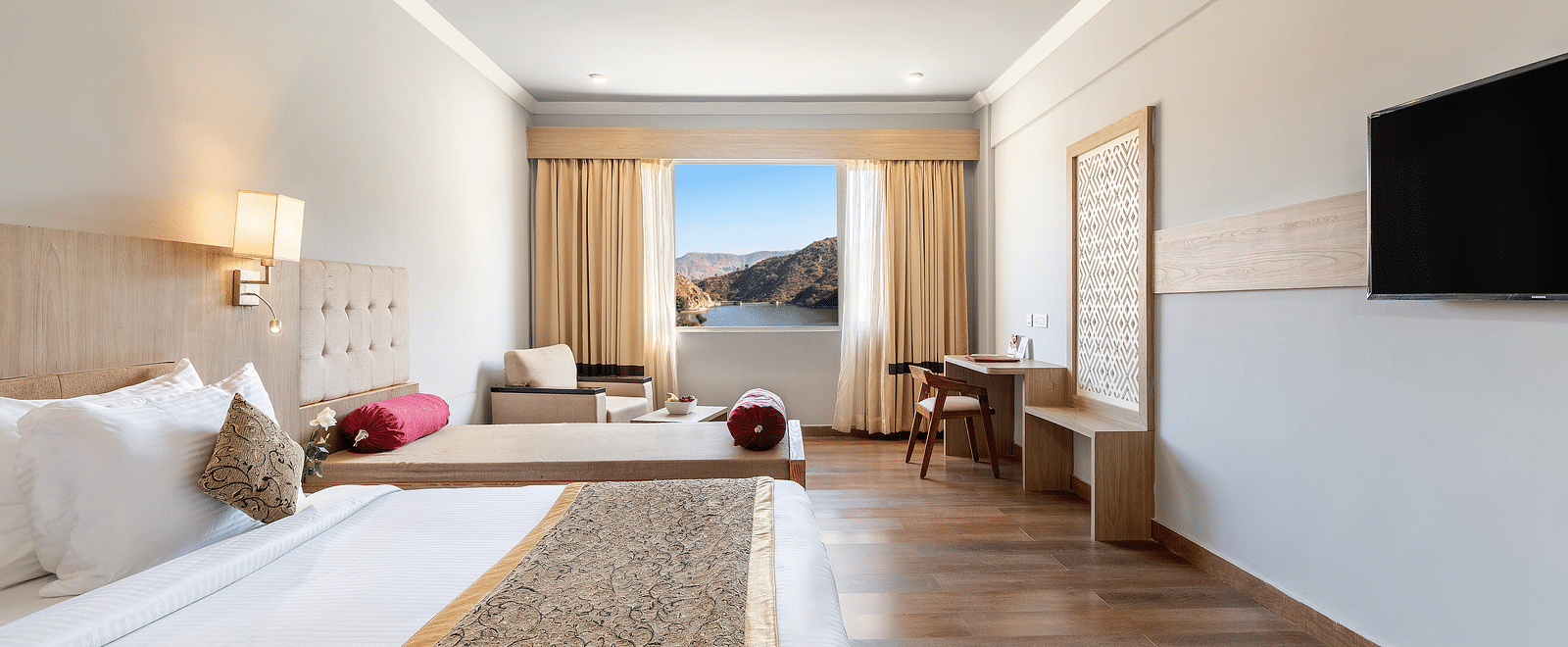 A close-up shot of a bed with a patterned runner on it, opposote to it is a tv mounted on the wall -  Via Lakhela Resort & Spa 