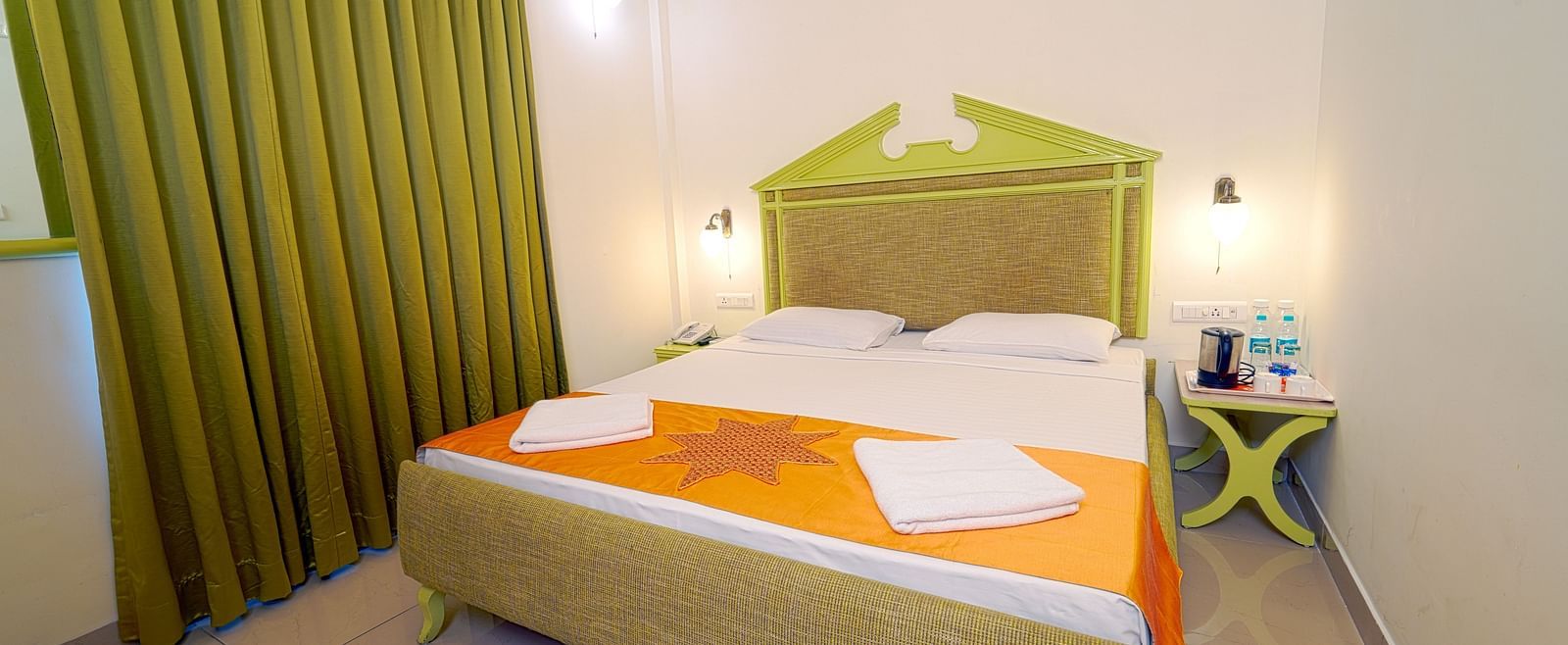 A hotel bedroom with a large double bed, green headboard, and green curtains, giving a cozy ambience at Greens Inn - Best Accommodation in Ramoji Film City.