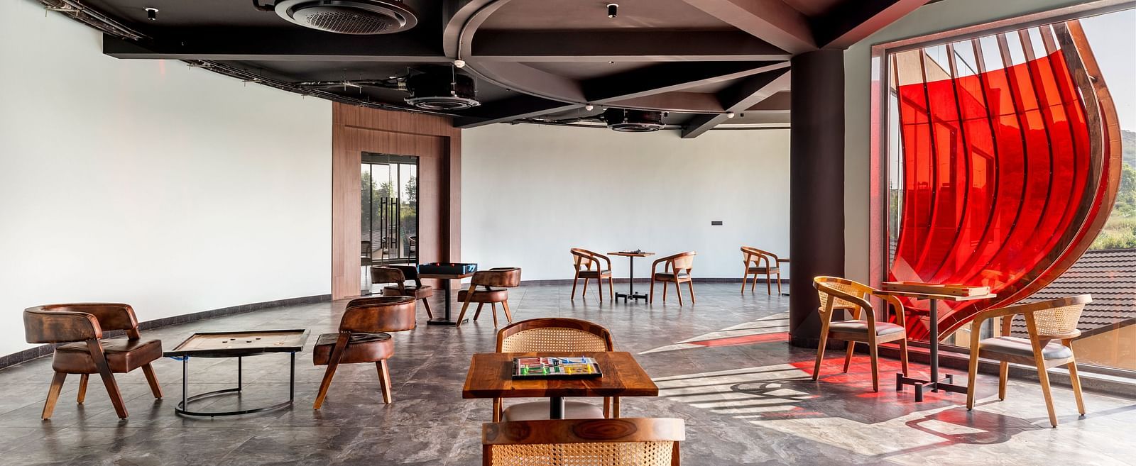An indoor games area at The Qualia Resort Club & Brewery, Udaipur featuring unique seating arrangements, a dark ceiling with track lighting, and a partial view of a red curtain.