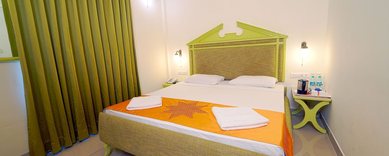A hotel bedroom with a large double bed, green headboard, and green curtains, giving a cozy ambience at Greens Inn - Best Accommodation in Ramoji Film City.