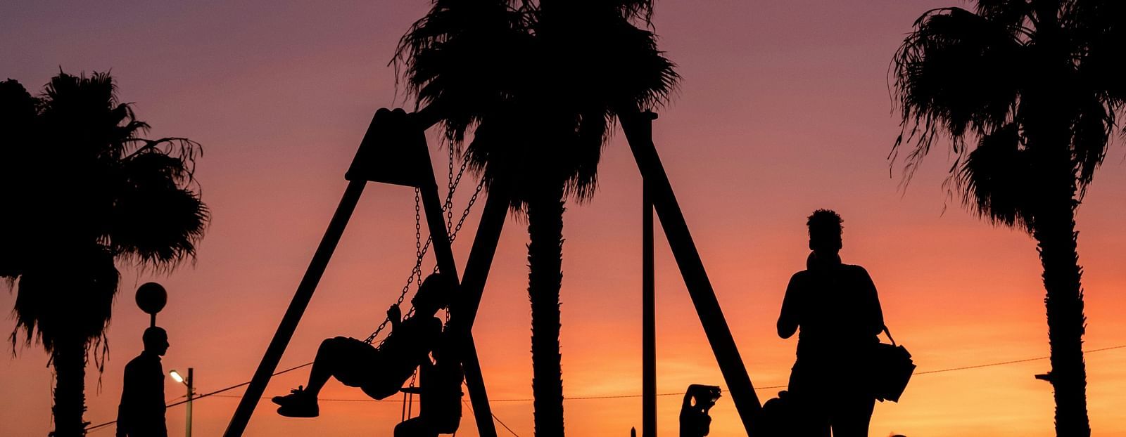 Silhouettes of people and palm trees against a sunset sky.