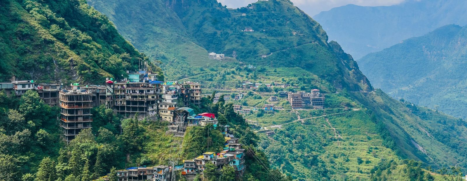Aerial view of mountains under daylight, featuring a few buildings in the stunning natural landscape.