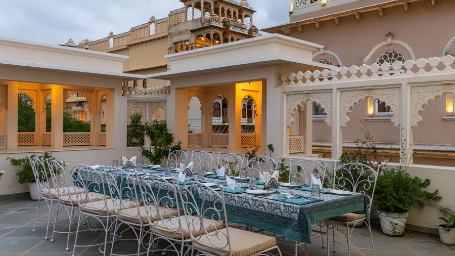 A long dining table with a tablecloth and chairs is arranged on an outdoor terrace at Akshay Niwas Boutique Hotel by Amantra, Udaipur.