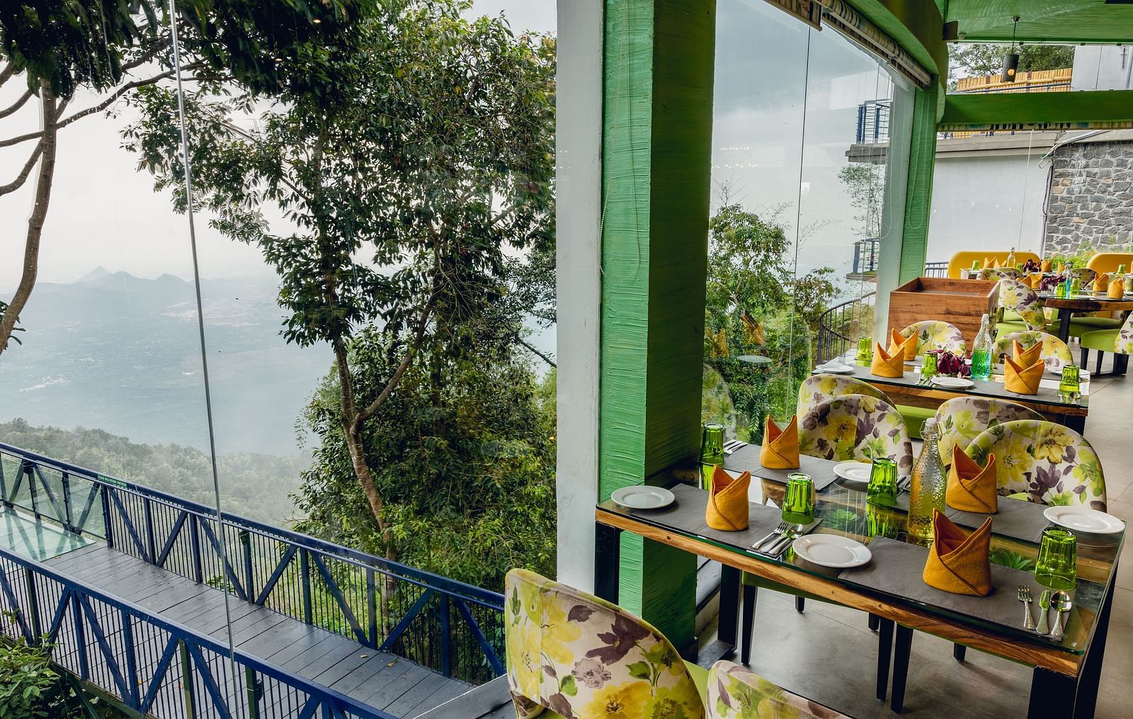An image of a restaurant with seating arrangement and expansive glass window over looking the serene mountains - Great Trails Yercaud by GRT Hotels