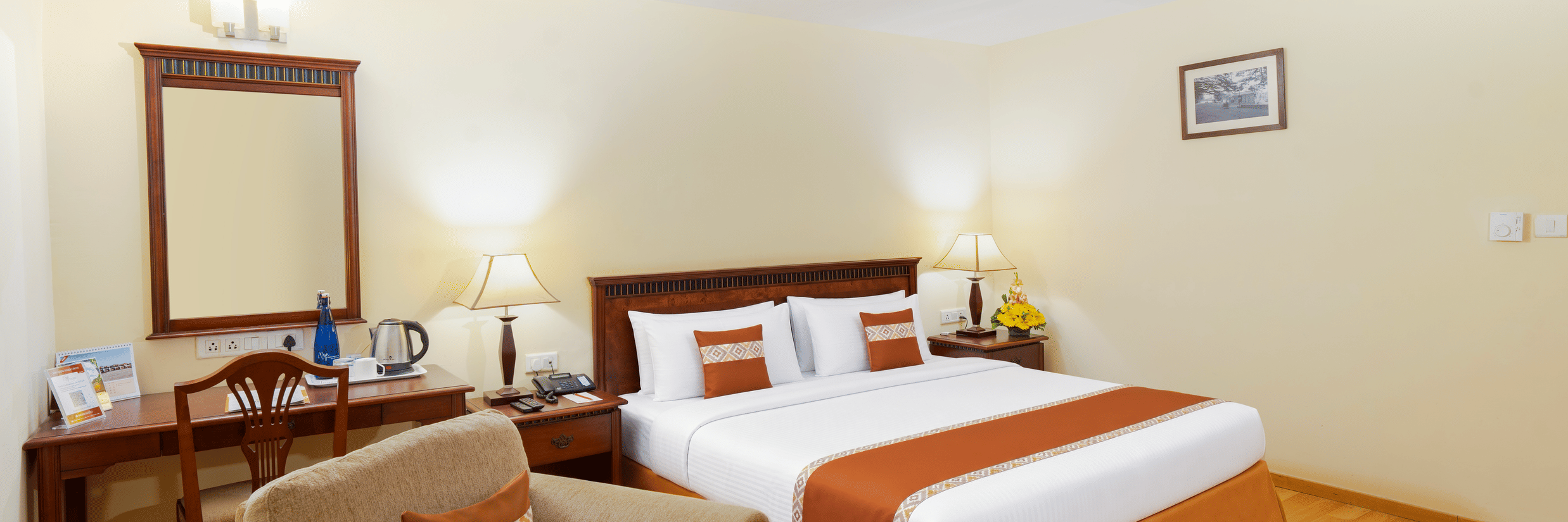 A room with a large bed, spreads, pillows, a sofa, a mirror, and lights. | MGM Mark Whitefield