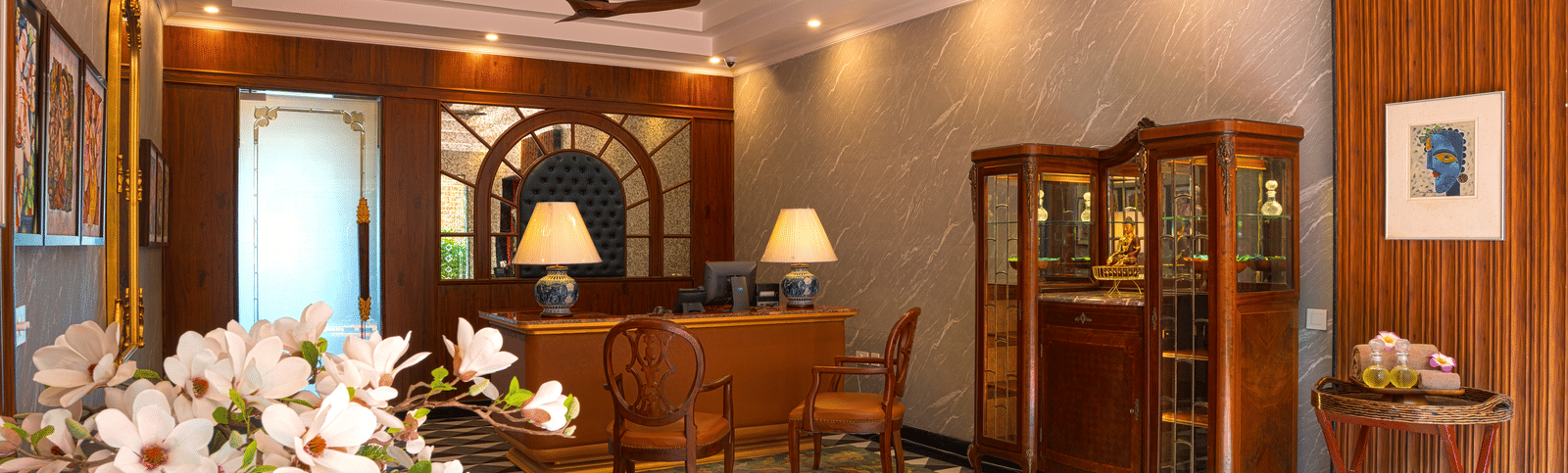 A lobby area with wooden furniture, decorative cabinetry, white flowers, and a geometric tiled floor at MAYFAIR Bay Resort, Paradeep.