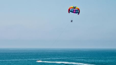 Parasailer soaring over the Sea and a motorboat creating a circular wake below in the sea.