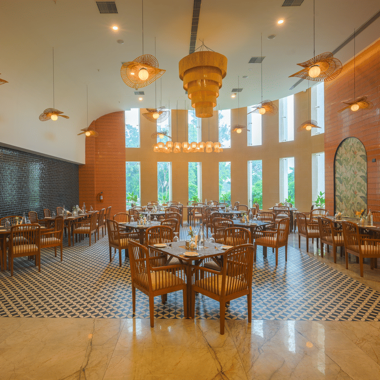 Restaurant dining area with wooden tables and chairs, pendant lights, decorative walls and large windows.